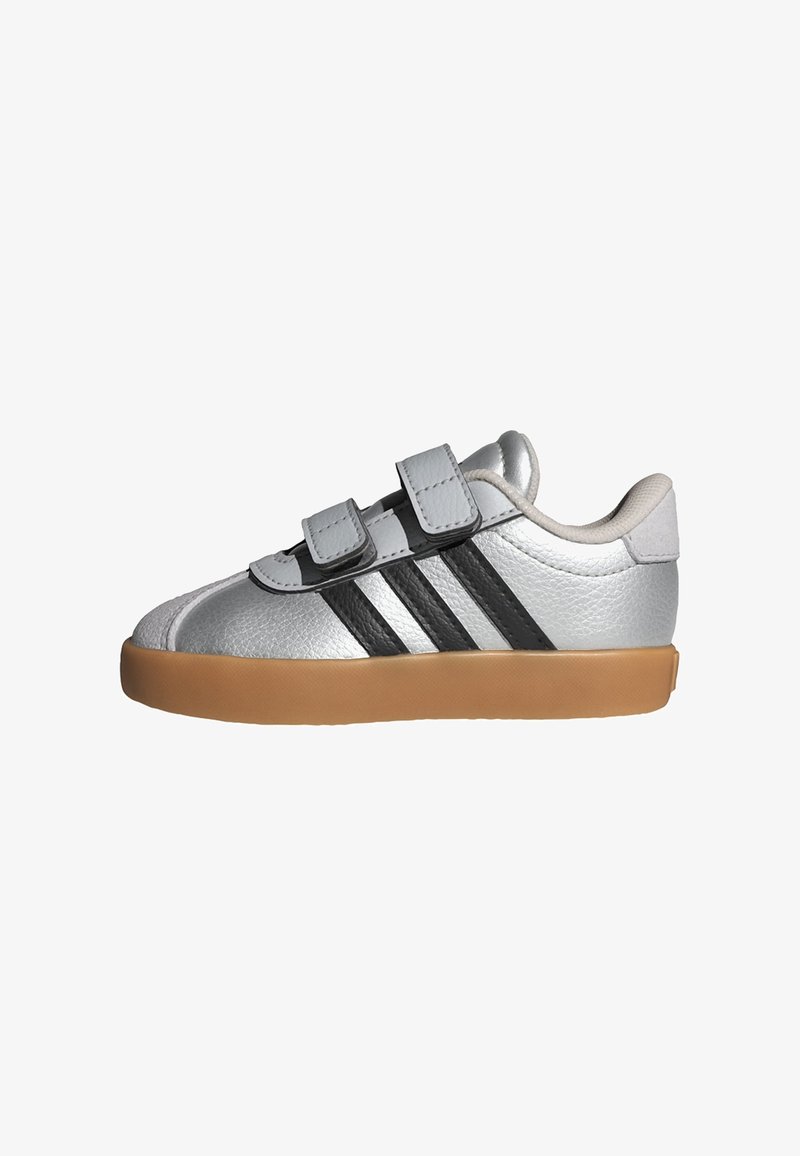 Strieborné kožené tenisky s dvoma čiernymi suchými zipsami, gumenou podrážkou a tromi čiernymi pruhmi po boku. Dizajn s guľatou špičkou.