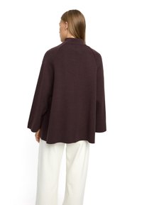 Ciemnobrązowy, teksturowany pulower z kołnierzem, raglanowymi rękawami i luźnym krojem. Noszony na kremowych szerokich spodniach.