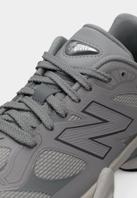 Gros plan d'une basket New Balance grise montrant des lacets texturés, un tissu en mesh et le numéro de modèle 9060 sur l'étiquette de la languette.