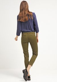 Oliwkowe dopasowane spodnie o skróconym kroju, z tylnymi kieszeniami. Zestawione z granatową bluzką, noszone z czarnymi butami typu slip-on.