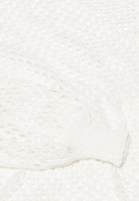 Witte gebreide stof met een los, open weefpatroon. De randen hebben een geribbelde textuur voor extra detail en structuur.