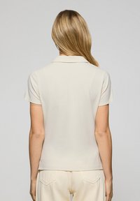 Polo a maniche corte di colore beige chiaro con colletto classico, realizzato in un morbido tessuto di cotone, presenta un orlo dritto e un design semplice.