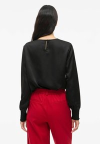 Blusa nera a maniche lunghe con scollatura rotonda e un piccolo dettaglio a chiave sul retro, abbinata a pantaloni rossi con vita elastica.