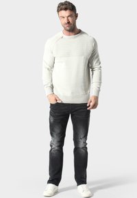 Helles graues Rundhals-Pullover mit gerippten Schulterdetails, kombiniert mit dunkelgrauen, verwaschenen Jeans und weißen Turnschuhen. Lässiger, körperbetonter Look.