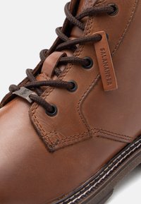 Brūni ādas potītes zābaki ar apaļām auklām, izšūtu dizainu un neilona birku ar "Salamander". Gumijas zole ar kontrastējošu šuvumu.