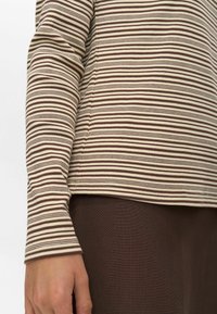 Kar és oldal torso egy világos háttér előtt, barna és bézs csíkos, hosszú ujjú ingben és egyszínű barna nadrágban.