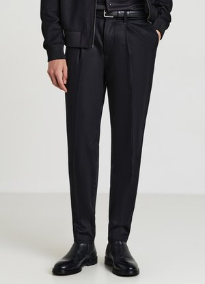 Pantaloni neri su misura con una texture morbida, vestibilità dritta e una lieve lucentezza. Abbinati a scarpe nere lucide e una giacca coordinata.