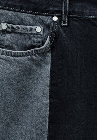 Tissu en denim avec une fente verticale ; côté gauche poche de jean gris clair avec rivets, côté droit panneau en jean noir uni.