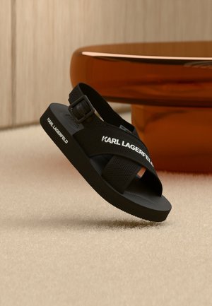 Schwarze offene Sandale mit verstellbarem Riemen, dicker Sohle und dem "KARL LAGERFELD" Logo auf den seitlichen Riemen und dem Sohlenrand.