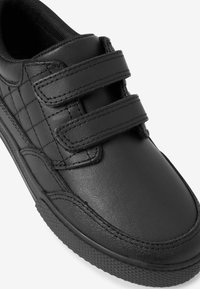 Sneaker en cuir noir avec double strap Velcro, détails texturés sur les côtés, col rembourré et semelle en caoutchouc à motif.