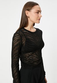 Maglia nera a maniche lunghe, lavorata a maglia, con un motivo testurizzato. Il tessuto presenta un design a trama aperta, che mostra la pelle sotto gli strati.