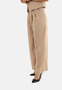 Pantalons larges beige en tissu lisse, avec des plis, associés à des chaussures à talons noirs brillantes.