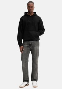 Felpa nera con cappuccio e tasca frontale, con un logo discreto. Abbinata a jeans grigi e sneakers bianche con dettagli neri.