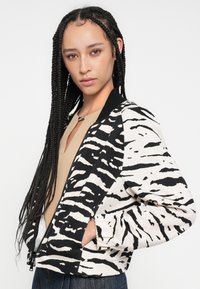 Veste bomber noir et blanc à imprimé zèbre avec fermeture éclair, poignets côtelés et poches latérales. Tissu doux avec une coupe décontractée.