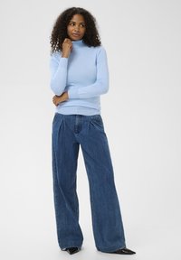 Pull ajusté col roulé bleu clair associé à un jean denim foncé à jambes larges. Le pull présente des poignets et un ourlet côtelés, tandis que le jean est orné de plis.