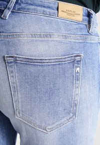 Ljusblå denimjeans med en blekt finish. Har en enda bakficka med en böjd form och en liten vit logotryck. Sliten textur är synlig.