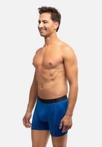 Modré boxerky vyrobené z hladkého materiálu. Mají černý pás se značkováním. Tvar je přiléhavý, sahající do poloviny stehna.
