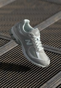 Light gray athletic shoe with mesh and suede materials; features a chunky sole, lacing system, and reflective accents.