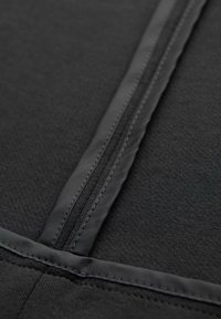 Gros plan d’un tissu noir avec une fermeture éclair verticale et des coutures cousues, montrant la texture et les détails de construction du matériau.
