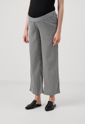 Pantaloni a gamba larga a righe in bianco e nero con una vita fitted; abbinati a scarpe slip-on nere. Tessuto morbido con righe verticali.