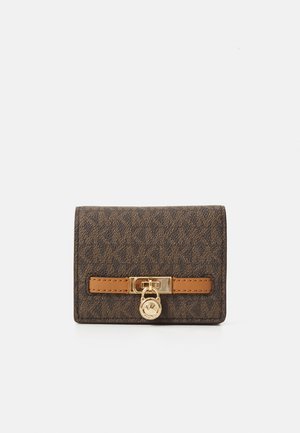 Compact brown monogram wallet with gold padlock detail and tan leather strap accent on white background.
