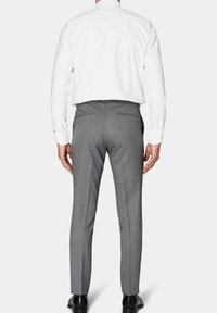 Pantaloni grigi su misura con vestibilità slim, tessuto testurizzato, tasche laterali e passanti per cintura, abbinati a una camicia bianca a maniche lunghe tinta unita.
