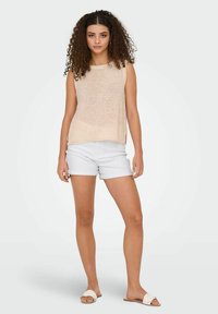Top senza maniche lavorato a maglia beige con vestibilità comoda, abbinato a pantaloni corti in denim chiaro. Il modello indossa sandali piatti con un design semplice.