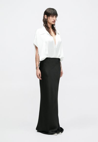Bijela satenska bluza s dubokim V-izrezom i širokim rukavima, u kombinaciji s elegantnom crnom satenskom suknjom. Suknja ima ravnu siluetu i suptilan rub.