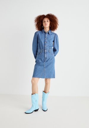Abito camicia in denim, azzurro chiaro, con apertura frontale a bottoni, maniche a palloncino, vita cintrata e gonna fino al ginocchio. Abbinato a stivali da cowboy azzurri chiari.