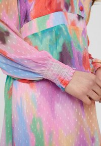 Robe transparente multicolore avec tissu texturé. Caractérisée par des manches bouffantes, des poignets froncés et un mélange de teintes vibrantes dans un motif aquarelle.