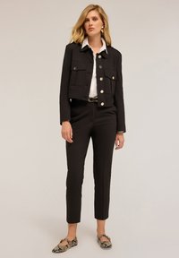 Sort cropped jakke med store forlommer og sølvhardware, parret med skræddersyede sorte bukser og snakemønstret flade sko. Hvid bluse underneath.