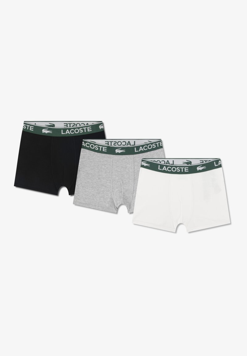 Tre par herre boxershorts i sort, grå og hvid, hver med en grøn linning med "LACOSTE"-logoen.