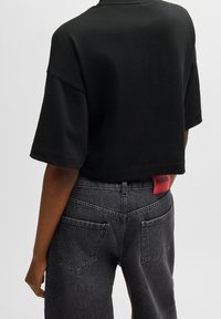 Czarny, krótki t-shirt z krótkimi rękawami. Szare dżinsy z wysokim stanem z czerwoną metką "HUGO" na tylnej stronie pasa. Teksturowany materiał.