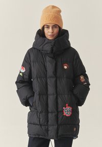 Juoda pūkinė striukė su aukštu apykakle, papuošta spalvingomis siuvinėtomis gėlėmis ir personažais ant rankovių ir priekinės dalies.