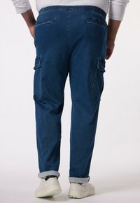 Niebieskie dżinsowe spodnie cargo o luźnym kroju, z elastyczną talią, mankietami u dołu oraz licznymi kieszeniami. Gładka tekstura i mocne detale szwów.