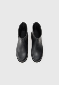 Bottines noires en caoutchouc avec une finition lisse, présentant des bouts ronds et des panneaux latéraux élastiques pour un enfilage facile.