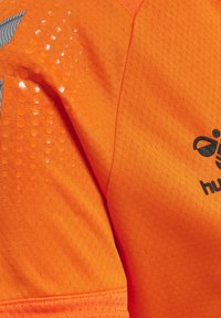 Oranje sportshirt van textuurstof met glanzende stippenaccenten en een logo. Het ontwerp bevat een geometrisch patroon op de schouder.