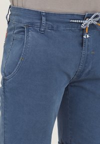 Blue denim shorts with a textured finish, featuring a drawstring in a contrasting pattern, side pockets, and visible stitching details.