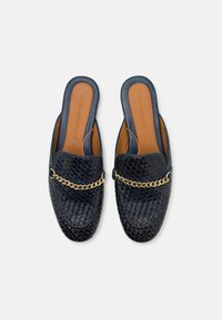 Marina vävda lädermules har en guldkedjeaccent över toppen och en brun läderinnersula. Slip-on-design med öppen häl.