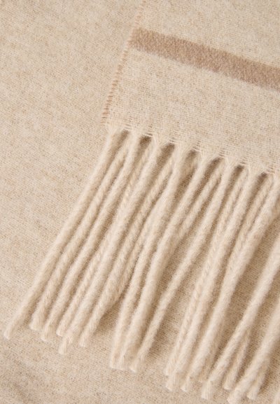 Détail d'une écharpe en laine beige douce montrant des franges et un motif rayé subtil sur le tissu.