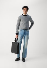 Grijze gebreide trui met zwarte accenten, lichtblauwe jeans, zwarte leren schoenen, houdt een rechthoekige zwarte tote bag vast. Eenvoudig ontwerp, ontspannen pasvorm.