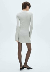 Abito lavorato a maglia di colore grigio chiaro, con una texture a coste, maniche lunghe e orlo a zigzag. Abbinato a collant neri trasparenti e scarpe nere a punta.