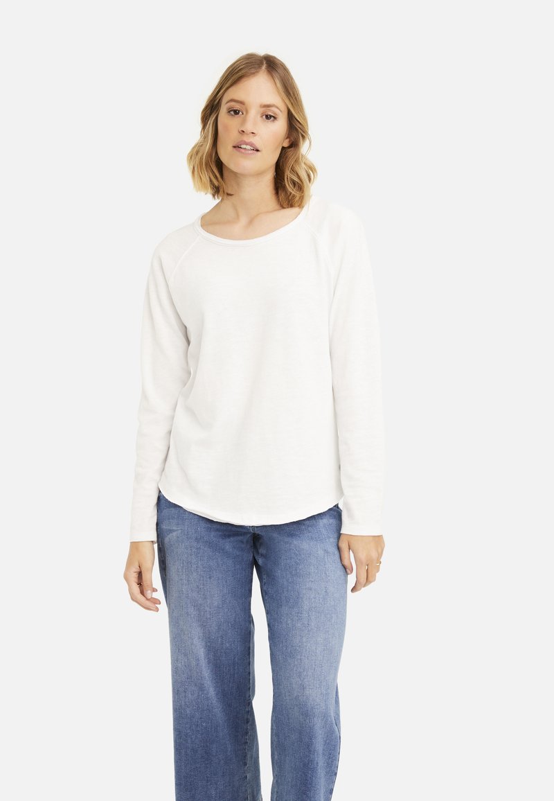 Weißes Langarmshirt mit rundem Halsausschnitt und Raglanärmeln, kombiniert mit blauen weit geschnittenen Jeans. Glatte Textur, lässiges Design.