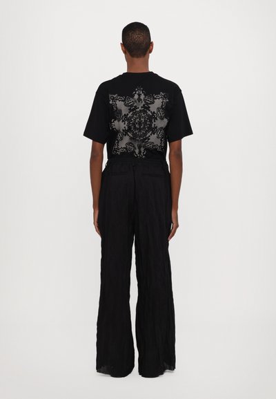 Camiseta negra con un intrincado patrón floral gris en la parte trasera, combinada con pantalones negros sueltos y texturizados.