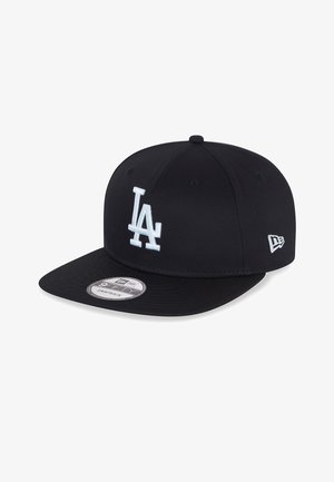 Gorra de béisbol negra hecha de tela con visera plana. Presenta un logotipo bordado en blanco de "LA" en la parte frontal y un acento blanco en el lado.