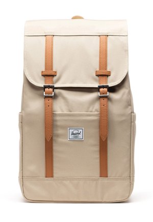 Sac à dos beige avec rabat avant sécurisé par deux sangles marron clair et boucles argentées, doté d'une poche avant avec une étiquette de la marque Herschel.
