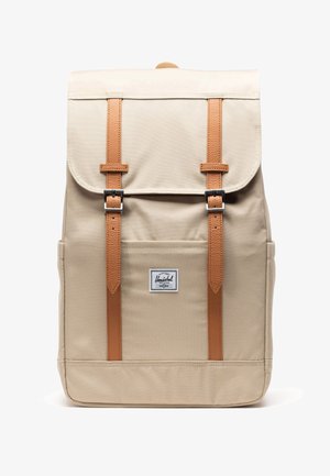 Mochila beige con solapa frontal asegurada por dos correas marrones y hebillas plateadas, que cuenta con un bolsillo delantero con una etiqueta de la marca Herschel.