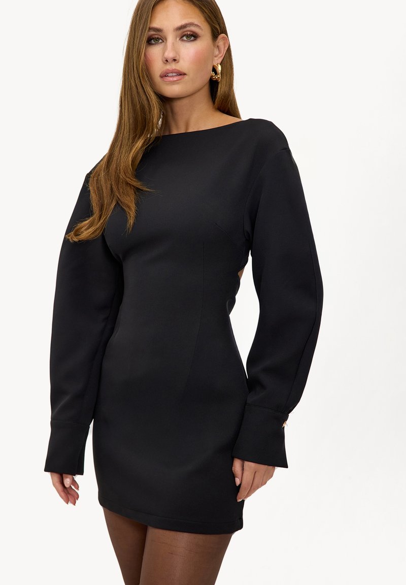 Robe mini noire en tissu structuré, avec manches longues, encolure bateau et silhouette droite agrémentée de détails subtils de coutures.