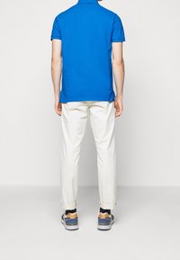 Niebieska koszulka polo, białe spodnie i trampki. Polo ma krótkie rękawy; spodnie są wywinięte na mankietach. Trampki mają pomarańczowe akcenty.