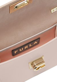 Borsa a mano in pelle rosa chiaro con chiusura in tono oro. L'interno presenta una texture in suede liscia e un rivestimento a righe rosa con etichetta nera Furla.